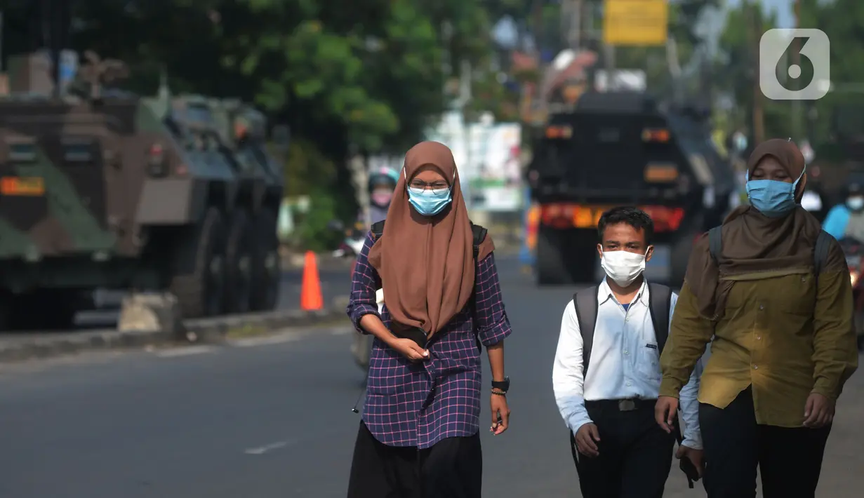 Warga berjalan dengan latar belakang kendaraan taktis jenis barracuda dan panser yang disiagakan di pos penyekatan di Jalan Raya Bogor, Jakarta, Selasa (6/7/2021). Petugas Gabungan Polri dan TNI menyiapkan kendaraan taktis untuk membantu penyekatan selama PPKM Darurat. (merdeka.com/Imam Buhori)