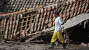 Di beberapa titik, jalan desa tertimbun material vulkanik hingga setinggi atap rumah. Tampak dalam foto, seorang pria menyelamatkan barang-barang dari sebuah rumah yang hancur akibat aliran piroklastik Gunung Semeru di Desa Supiturang, Lumajang, Jawa Timur, pada Jumat 21 November 2025. (Agus Harianto/AFP)