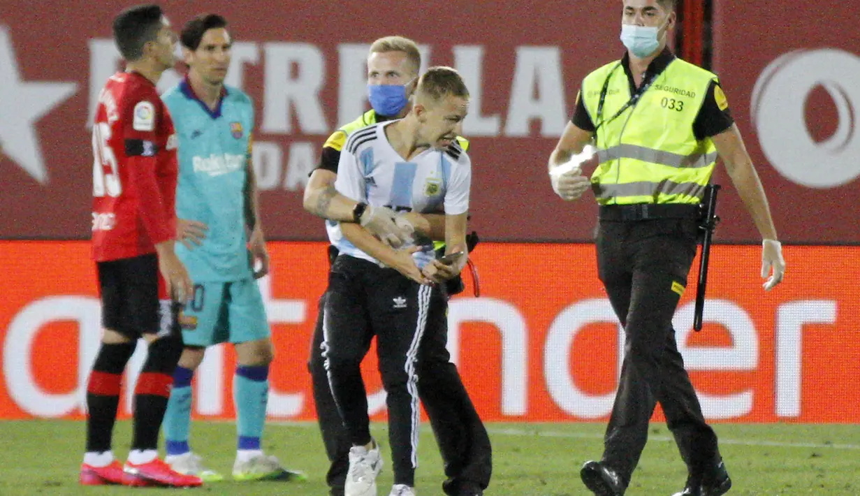 Petugas keamanan menangkap seorang penyusup yang masuk ke lapangan saat pertandingan La Liga antara Mallorca dengan FC Barcelona di Son Moix Stadium, Palma de Mallorca, Spanyol, Sabtu (13/6/2020). Dalam pertandingan tersebut Barcelona mengalahkan Mallorca dengan skor 4-0. (AP Photo/Francisco Ubilla)