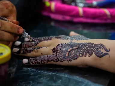 Seorang ahli kecantikan melukis 'Henna' tradisional di tangan pelanggan untuk perayaan Idul Fitri, yang menandai berakhirnya bulan suci Ramadan, di Rawalpindi, Pakistan, Rabu 18 Maret 2026. (AP Photo/Anjum Naveed)