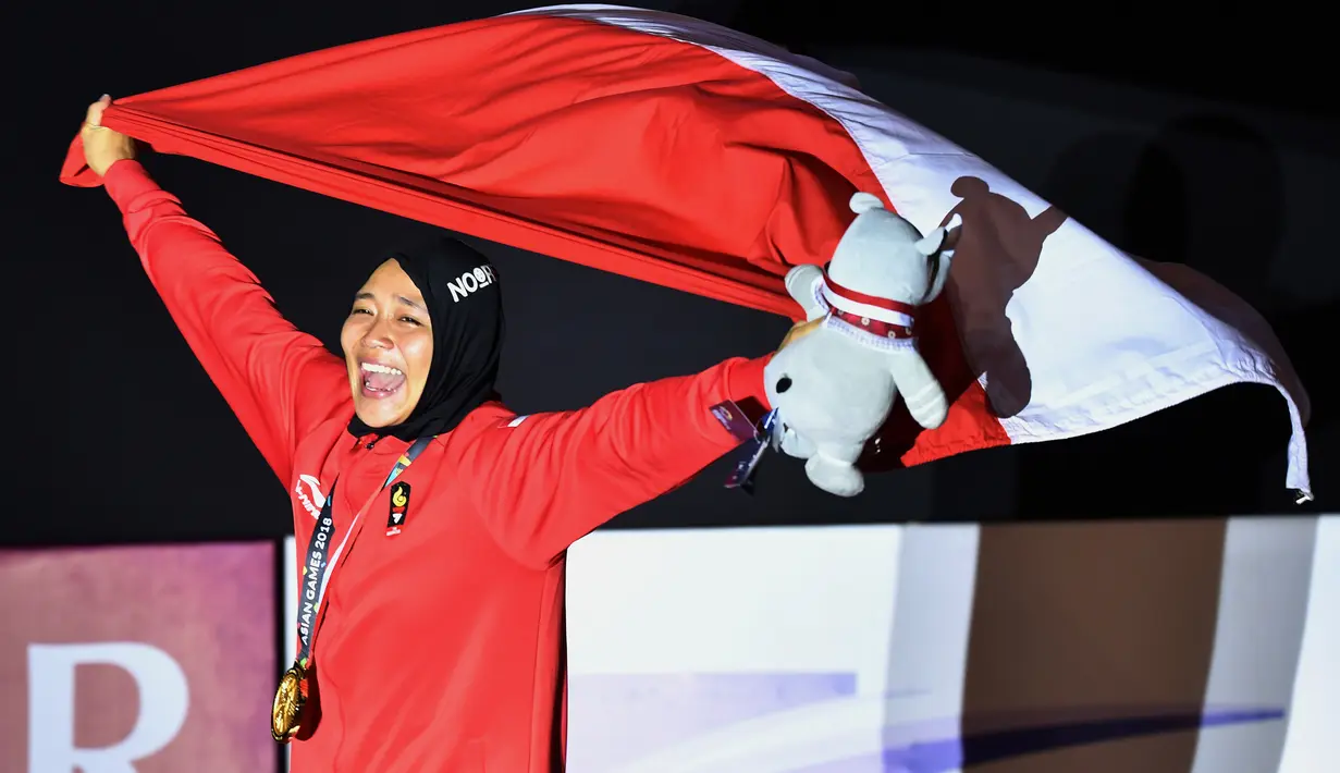 Peraih medali emas Indonesia Susanti Rahayu Aries membawa bendera merah putih pada upacara penyerahan medali olahraga panjat tebing wanita Asian Games 2018 di Palembang (23/8). (AFP PHOTO / Adek Berry)