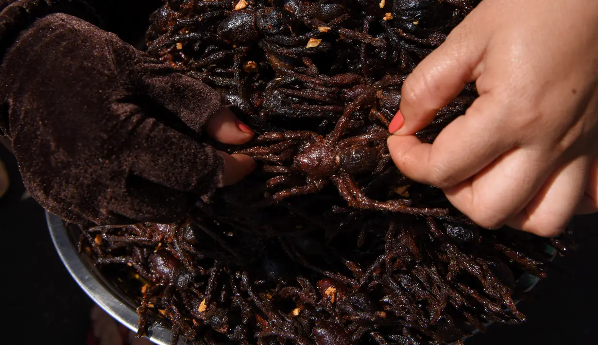 Pedagang Kamboja menyiapkan tarantula goreng untuk dijual di wilayah Skun, Provinsi Kampong Cham, 4 Desember 2019. Daerah yang kerap dijuluki "Spiderville" tersebut menjadi tempat menarik bagi para turis berburu aping, camilan tradisional dari tarantula ini. (TANG CHHIN Sothy / AFP)