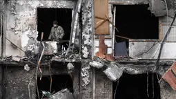 Seorang prajurit Ukraina terlihat di jendela bangunan tempat tinggal yang rusak di Koshytsa Street, pinggiran ibukota Ukraina Kiev (25/2/2022). Presiden Ukraina Volodymyr Zelensky mengatakan pasukan penyerang menargetkan warga sipil dan ledakan terdengar di ibu kota yang terkepung. (AFP/Daniel Leal)