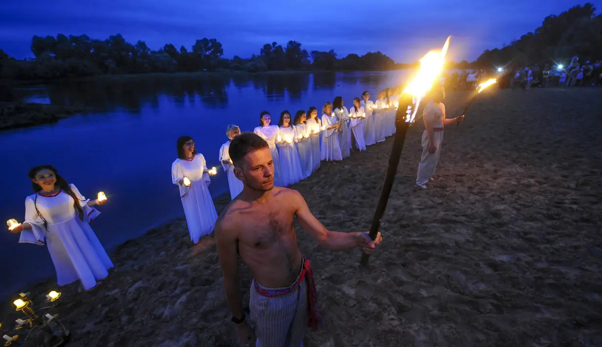Pemuda Belarusia memegang lilin dan obor berdiri di Sungai Berezina pada Hari Ivan Kupala di Desa Parichi, sekitar 200 km (125 mil) selatan Parichi, Belarusia, 6 Juli 2022. Hari Ivan Kupala merupakan sebuah perayaan malam kuno yang menandai Titik Balik Matahari Musim Panas, malam terpendek tahun ini. (AP Photo/Viktor Drachev)