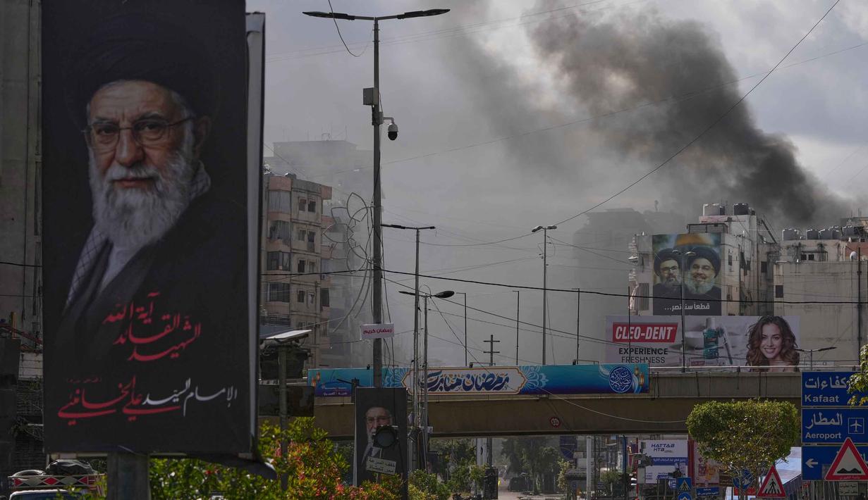 Kepulan asap terlihat di balik potret mendiang Pemimpin Tertinggi Iran, Ayatollah Ali Khamenei, setelah serangan udara Israel di Dahiyeh, pinggiran selatan Beirut, Lebanon, Senin, 30 Maret 2026. Serangan udara Israel kembali menghantam wilayah Dahiyeh, pinggiran selatan Beirut, Lebanon. (AP Photo/Hassan Ammar)