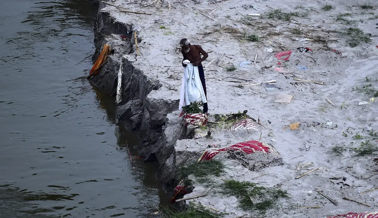 Seorang pria berjalan di tengah kuburan dangkal di pasir, beberapa di antaranya diduga orang yang meninggal karena virus corona COVID-19, dekat tempat kremasi di tepi Sungai Gangga, Phafamau, Allahabad, India, Sabtu (5/6/2021). (SANJAY KANOJIA/AFP)