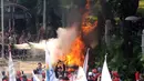 Polisi berupaya memadamkan karangan bungan yang dibakar saat aksi perayaan MayDay di Jalan Medan Merdeka Barat, Senin (5/1). Ribuan massa buruh turun ke jalan dalam perayaan Hari Buruh Internasional. (Liputan6.com/Helmi Fithriansyah)