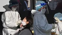Petugas medis (kiri) mengambil sampel usap hidung dari seorang wanita di pusat pengujian virus corona COVID-19, Seoul, Korea Selatan, Rabu (16/2/2022). Kasus COVID-19 harian Korea Selatan meningkat tajam mencapai angka tertinggi baru yaitu lebih dari 90 ribu. (Jung Yeon-je/AFP)