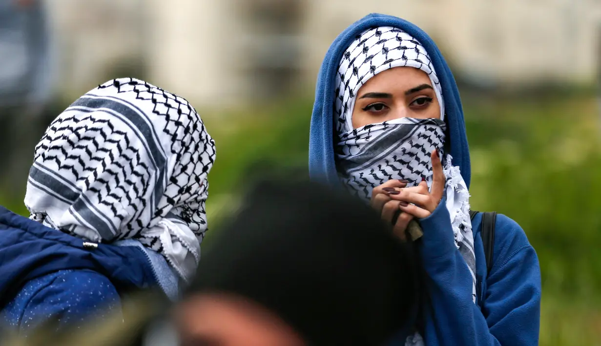 Seorang wanita Palestina menutupi wajahnya dengan kaffiyeh selama bentrokan dengan tentara Israel dalam demonstrasi untuk memperingati Hari Tanah di Tepi Barat, Sabtu (30/3).(Photo by ABBAS MOMANI/AFP)