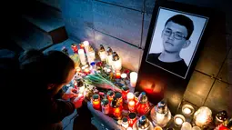 Seorang pria menyalakan lilin di depan foto Jan Kuciak di Bratislava (26/2). Pembunuhan itu terjadi di tengah pembuatan laporan investigatif Kuciak soal kasus dugaan kecurangan pajak yang melibatkan pengusaha. (AFP Photo/Vladimir Simicek)