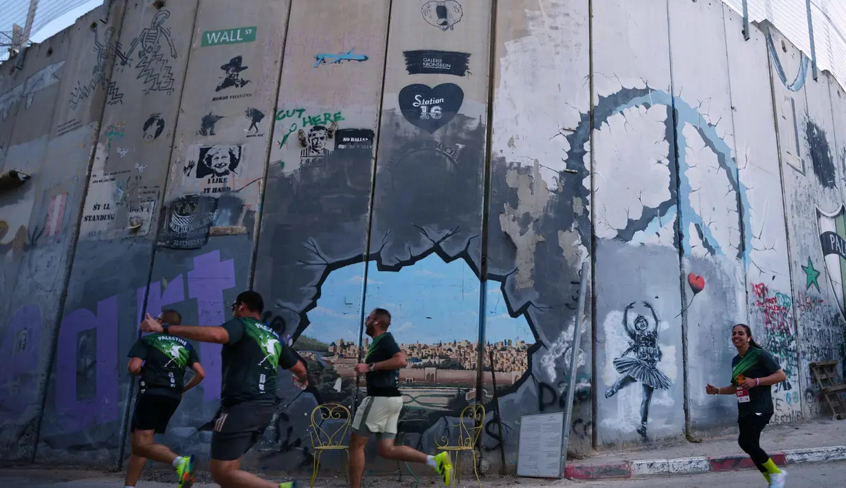 Edisi ke-10 acara ini menandai kembalinya Maraton Internasional Palestina ke jalanan Betlehem setelah sempat terhenti selama dua tahun akibat perang di Gaza. Tampak dalam foto, para pelari melewati tembok pemisah Israel saat mereka berkompetisi dalam Maraton Palestina di kota Betlehem, Tepi Barat, Jumat 8 Mei 2026. (AP Photo/Mahmoud Illean)