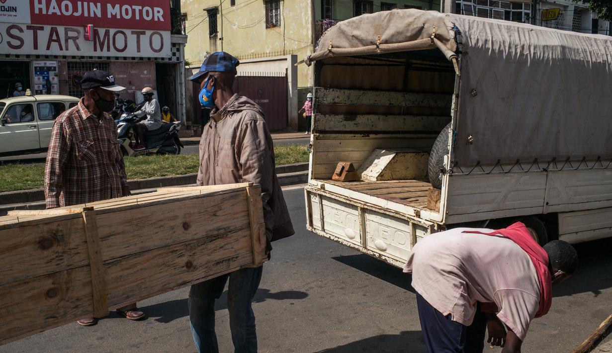 Tukang kayu memasukkan peti mati yang telah dipesan ke mobil di jalan raya umum, di Antananarivo, Madagaskar, Rabu (14/4/2021). Selama tiga minggu terakhir, Pak Jean dan timnya memproduksi antara 15 hingga 20 peti mati per hari, padahal sebelumnya hanya 3 atau 4 peti mati per hari. (RIJASOLO/AFP)
