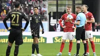 Wasit tengah berbincang dengan para pemain SC Freibugr dan Bayern Munchen pada lanjutan Bundesliga 2021/2022. Laga sempat terhenti akibat jumlah pemain Bayern Munchen di lapangan mencapai 12 orang. (AFP/Thomas Kienzle)