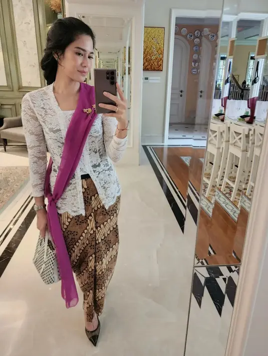 Tampil ayu, sekali lagi, Dian Sastro melakukan mirror selfie dalam balutan kebaya brokat putih, yang dipadunya dengan kain batik sebagai bawahan. Ia juga menyampirkan selendang ungu, bros emas yang disematkan di dadanya, dan menenteng hand bag berwarna hitam-putih. Foto: Instagram.