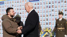 Presiden Ukraina Volodymyr Zelensky (kiri) menyambut dan menyalami Presiden AS Joe Biden (tengah) saat setelah tiba di Kyiv, Ukraina pada 20 Februari 2023. Zelensky menyambut gembira kunjungan Presiden AS Joe Biden. Biden bertemu dengan Presiden Ukraina Volodymyr Zelensky di ibu kota Ukraina,  dalam kunjungan pertamanya ke negara itu sejak dimulainya konflik. (Dimitar DILKOFF/AFP)