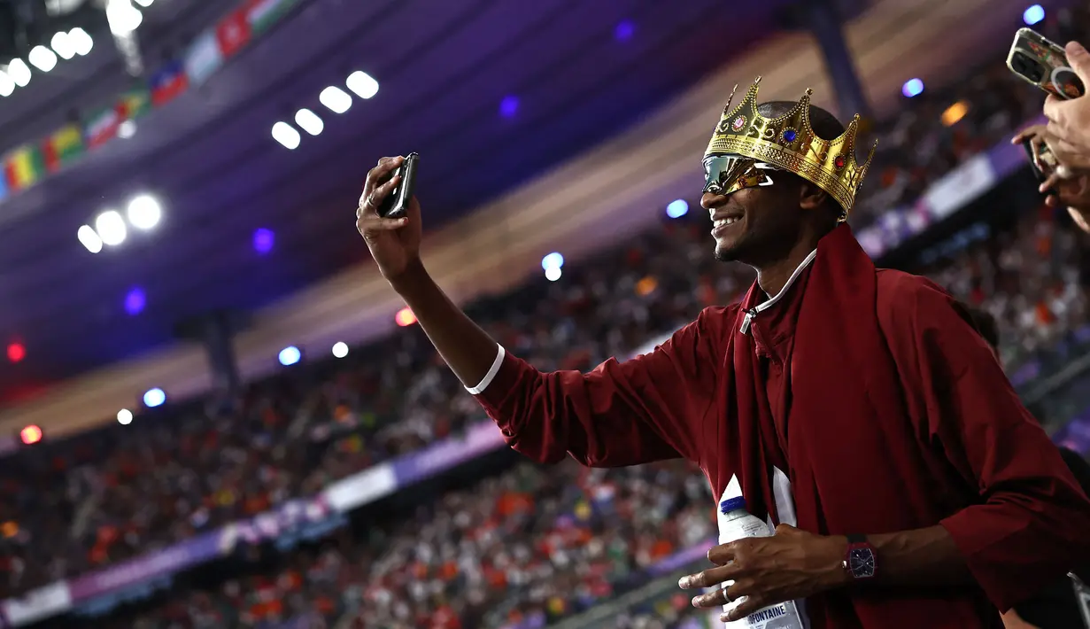 Atlet Qatar, Mutaz Barshim melakukan swafoto sambil mengenakan mahkota di kepalanya setelah pertandingan final cabang olahraga lompat tinggi Olimpiade Paris 2024 di Stade de France, Paris, Prancis, Sabtu (10/08/2024) waktu setempat. Ia berhasil mendapatkan medali perunggu dengan lompatan setinggi 2,34 meter. (AFP/Anne-Christine Poujoulat)