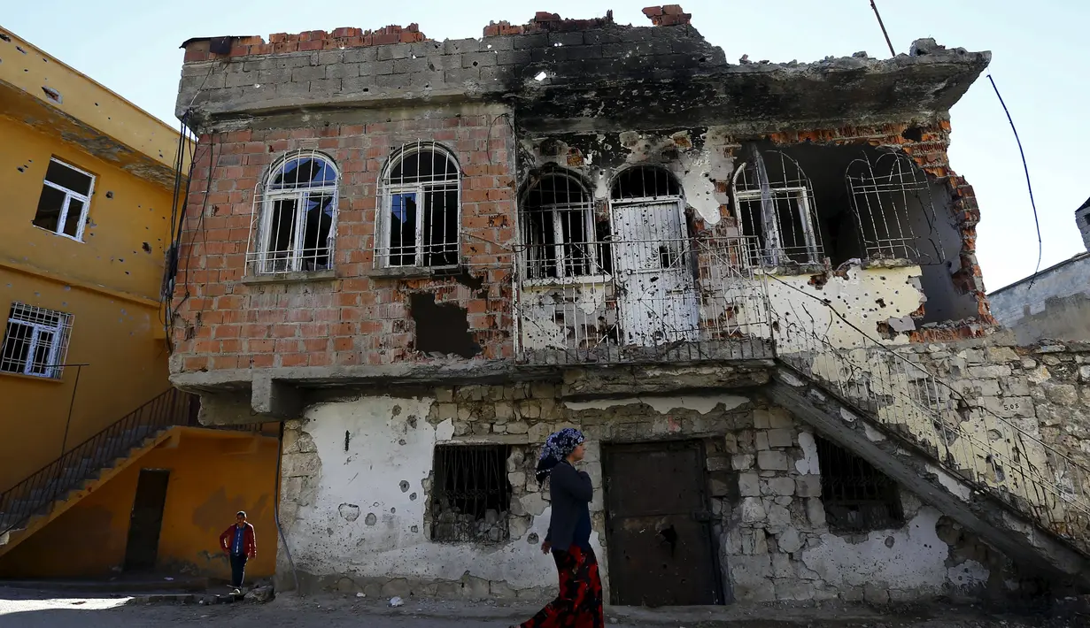 Seorang wanita berjalan melewati bangunan yang rusak akibat konflik antara Militer Turki dan Militan Kurdi di provinsi Diyarbakir, Turki, (7/12). Konflik ini telah terjadi puluhan tahun. (REUTERS/Murad Sezer)