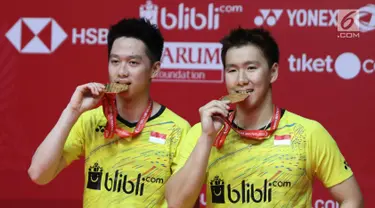 Ganda putra Indonesia Kevin Sanjaya Sukamuljo dan Marcus Fernaldi Gideon menggigit medali emas seusai mengalahkan ganda putra Cina Li Junhui dan Liu Yuchen pada babak final Indonesia Masters 2018 di Jakarta, Minggu (28/1). (Liputan6.com/Angga Yuniar)