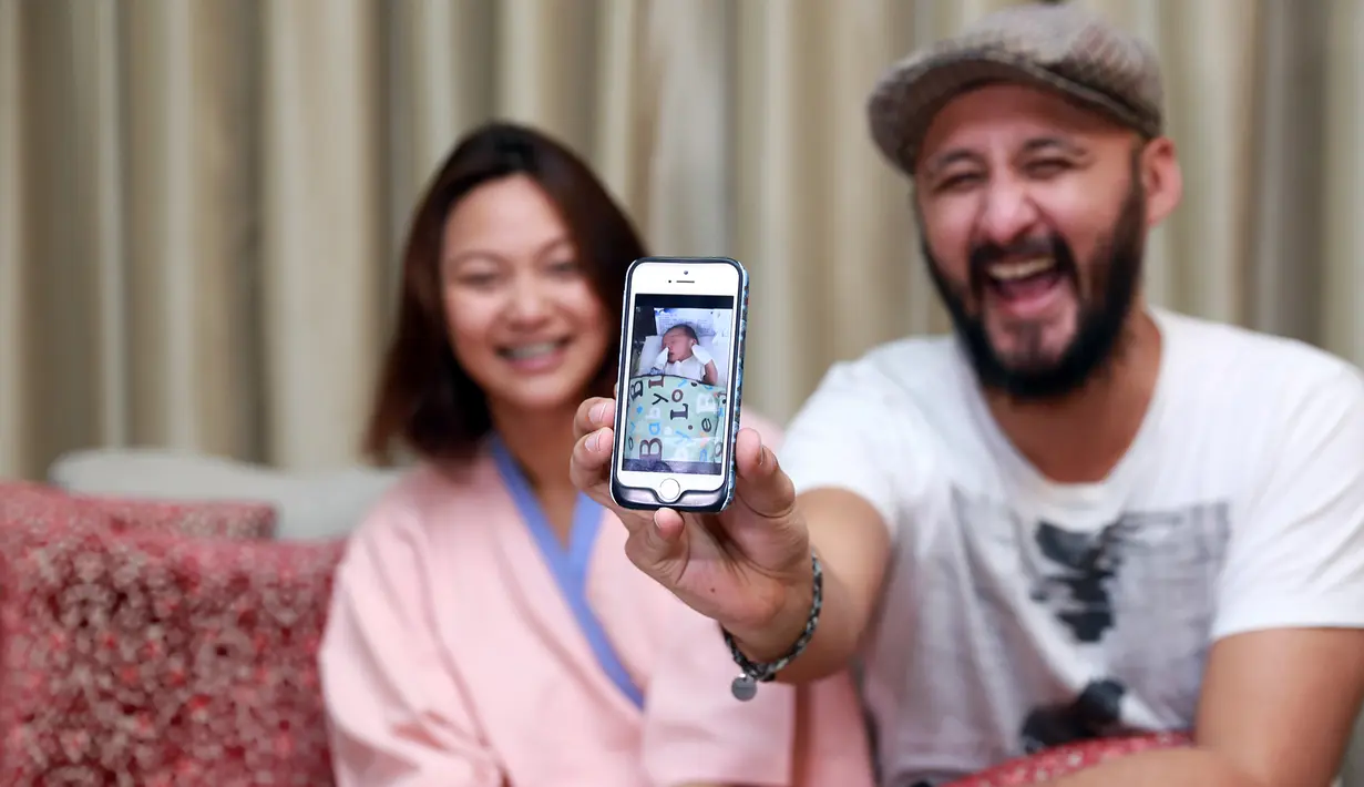 Ekspresi bahagia Aqi dan istri menunjukkan foto putra tercinta mereka. (Wimbarsana/Bintang.com)