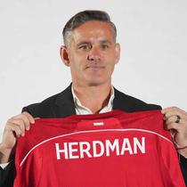 Sebagai informasi, John Herdman datang ke Indonesia dengan membawa sejumlah pengalaman sukses, terutama saat bertugas di Kanada. Dia mengantar timnas putri Kanada meraih dua medali perunggu berturut-turut dalam Olimpiade 2012 dan 2016. Tampak dalam foto, pelatih kepala tim nasional sepak bola Indonesia yang baru, John Herdman memegang jersey tim yang bertuliskan namanya saat konferensi pers di Jakarta, Selasa 13 Januari 2026. (AP Photo/Achmad Ibrahim)