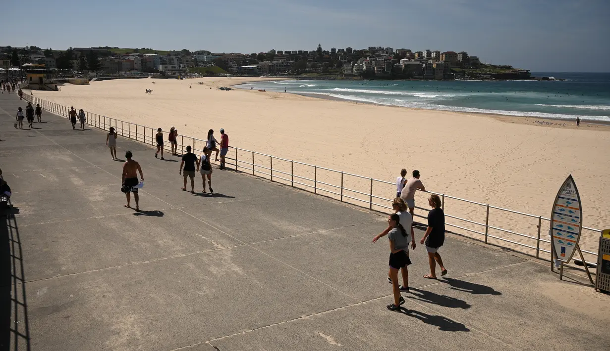 Orang-orang berjalan melewati Pantai Bondi yang kosong setelah ditutup oleh pihak berwenang di Sydney, Minggu (22/3/2020). Otoritas Australia menutup Bondi Beach  lantaran orang-orang mengabaikan larangan tidak berkumpul dalam jumlah besar untuk menekan penyebaran virus corona. (PETER PARKS/AFP)
