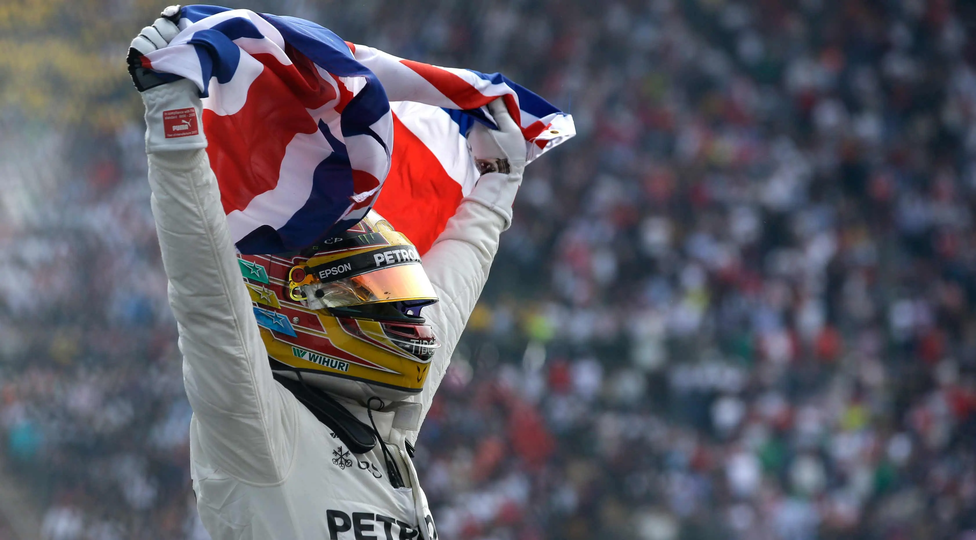 Lewis Hamilton membentangkan bendera negaranya saat merayakan kemenangannya meraih juara dunia F1 untuk yang ke empat kalinya di Autodromo Hermanos Rodrigue, Meksiko. (AP Photo / Moises Castillo)