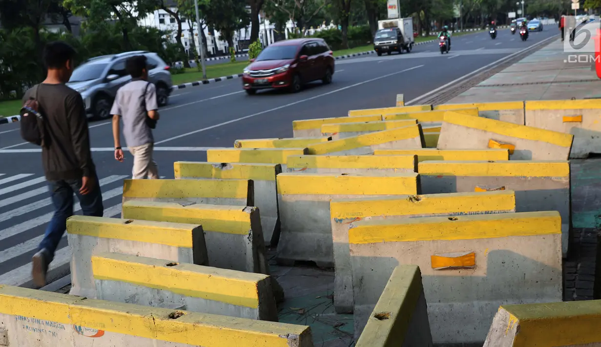 Pejalan kaki menghindari beton pembatas jalan yang diletakkan di atas trotoar Jalan Medan Merdeka Utara, Jakarta, Kamis (25/7/2019). Pembatas jalan yang berada tidak pada tempatnya mengganggu kenyamanan pejalan kaki yang melintasi trotoar jalan tersebut. (Liputan6.com/Helmi Fithriansyah)