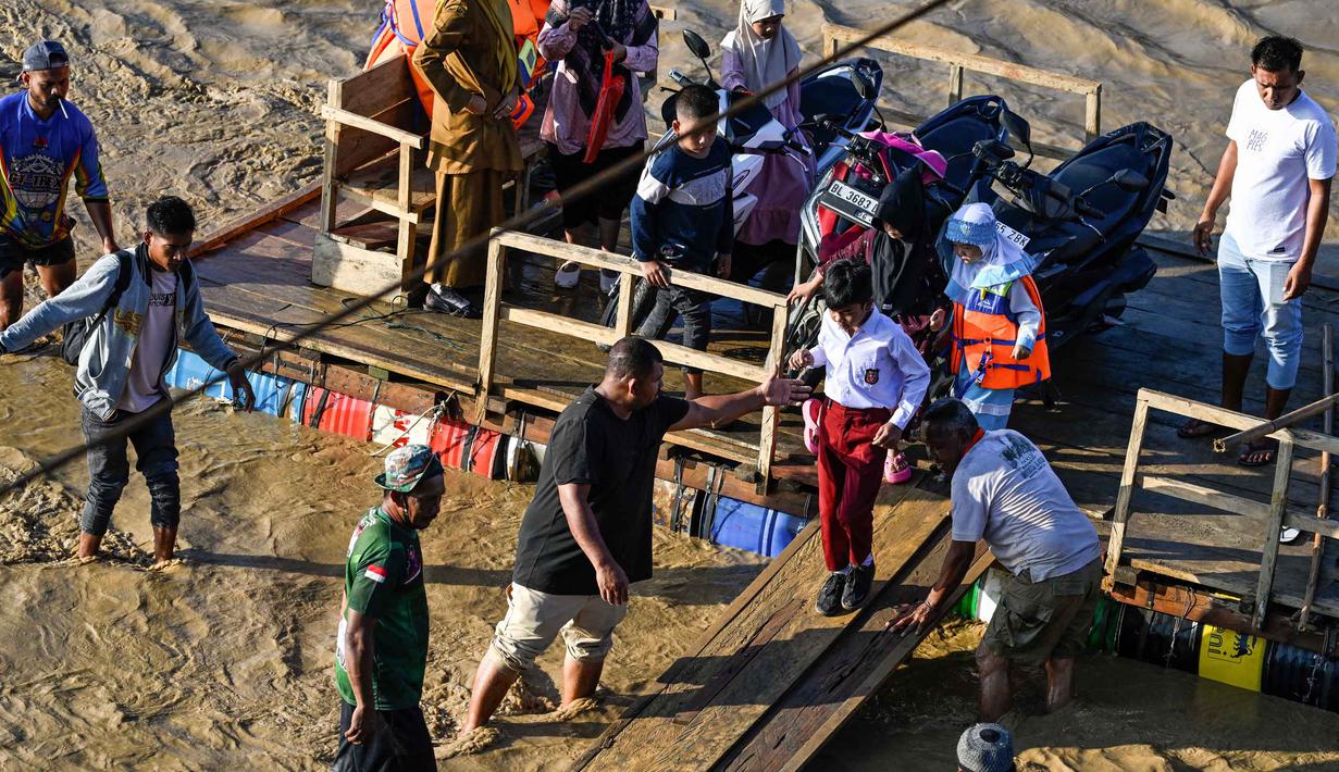 Rakit tali darurat tersebut menjadi alat penghubung utama bagi warga yang berada di dua sisi sungai untuk aktivitas ekonomi, pendidikan, serta keperluan sehari-hari. Tampak dalam foto, snak-anak turun dari rakit di sepanjang sungai Peusangan setelah banjir bandang yang menghancurkan desa-desa di sekitarnya di Kabupaten Bireuen, provinsi Aceh, pada Senin 5 Januari 2026. (CHAIDEER MAHYUDDIN/AFP)