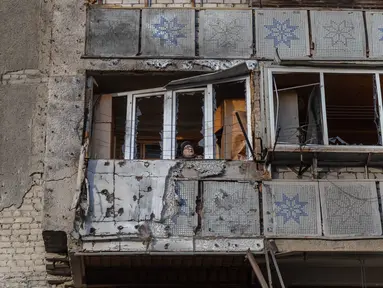Seorang wanita berdiri di balkon sebuah bangunan tempat tinggal yang rusak akibat serangan, di Odesa, pada 31 Desember 2025, di tengah invasi Rusia di Ukraina. Jelang pergantian tahun, Rusia kembali melancarkan serangan drone yang menyasar wilayah Odesa, Ukraina, Selasa (30/12/2025) malam waktu setempat. (Oleksandr GIMANOV/AFP)