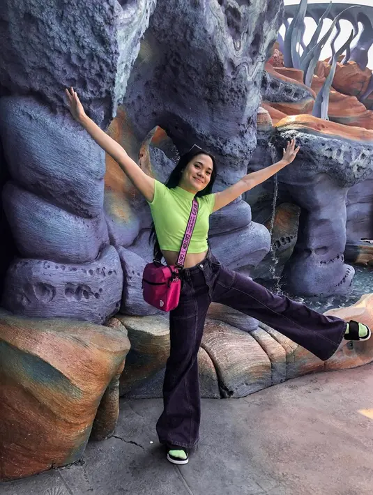 Perpaduan kaos dan kaos kaki hijau, serta celana berwarna ungu dan sling bag merah muda menjadi pilihan Sheryl saat berkunjung ke Tokyo Disney Sea. Senyum manis juga ditunjukan oleh Sheryl pada unggahan foto tersebut. (Liputan6.com/IG/@sherylsheinafia)