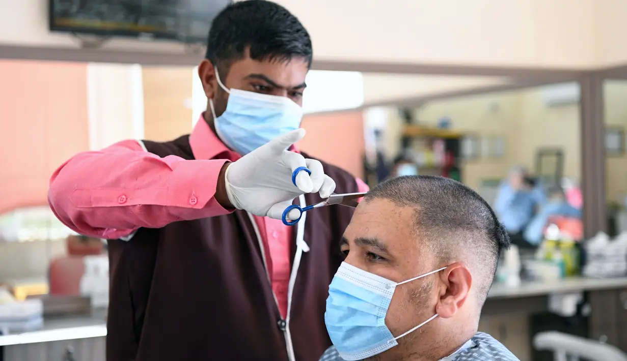 Seorang barber yang mengenakan masker memangkas rambut pelanggan di pasar Al-Mubarakiya di Kuwait City, Kuwait (18/8/2020). Kuwait mulai Selasa (18/8) memasuki tahap keempat dari rencana lima tahapnya untuk kembali ke kehidupan normal. (Xinhua/Ghazy Qaffaf)