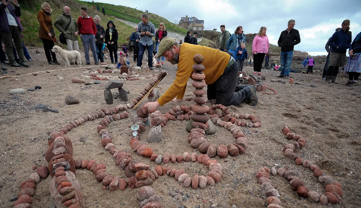 Seorang seniman saat membuat batu bertumpuk atau rock balancing dalam European Stone Stacking Championships 2018 di Dunbar, Skotlandia, Minggu (22/4). (ANDY BUCHANAN/AFP)