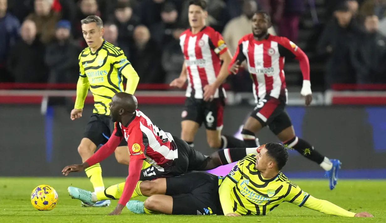 Bek Arsenal William Saliba, kanan bawah, berebut bola dengan gelandang Brentford Yoane Wissa pada pekan ke-13 Premier League 2023/2024, di Gtech Community Stadium, Minggu (26/11/2023) dini hari WIB. (AP Photo/Kirsty Wigglesworth)