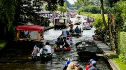 Wisatawan menaiki perahu menyusuri sungai di Giethoorn yang menjadi tujuan wisata favorit di Belanda pada 6 Agustus 2019. Mendapat julukan 'Venice of the North', kota tersebut menggunakan kanal-kanal sebagai jalan dan lalu lalang transportasi sehari-hari. (Robin van Lonkhuijsen/ANP/AFP)