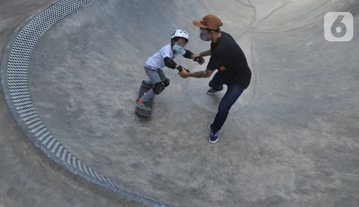 Instruktur melatih seorang anak menggunakan skateboard dengan memakai masker dan face shield di Crooz Shophouse di kawasan Duren Tiga, Jakarta Selatan, Minggu (2/8/2020). Mereka kembali melakukan latihan seminggu dua kali dengan menerapkan protokol kesehatan. (merdeka.com/Arie Basuki)