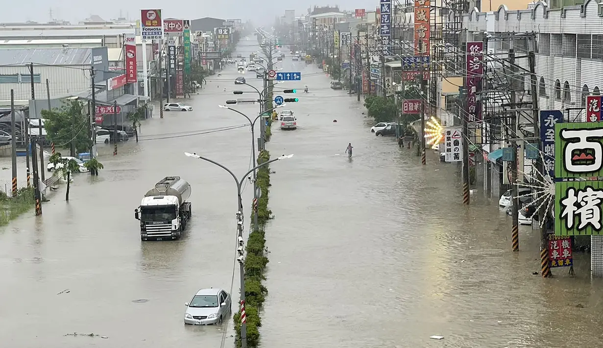 Orang-orang dan kendaraan menyeberangi air di sepanjang jalan yang tergenang banjir akibat Topan Gaemi di Kaohsiung, Taiwan pada tanggal 25 Juli 2024. ((Johnson LIU/AFP)