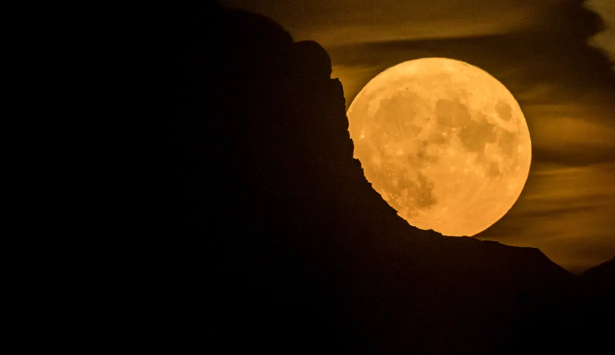 Bulan super purnama, muncul di balik gunung di Pegunungan Alpen Swiss, terlihat dari Chexbres, Swiss barat, Rabu (13/7/2022). Bulan Purnama dikenal sebagai Buck Moon dan juga Supermoon. Di kondisi ini Bulan akan terlihat tampak lebih besar dan terang sehingga terasa sangat dekat dari Bumi. (Fabrice COFFRINI / AFP)