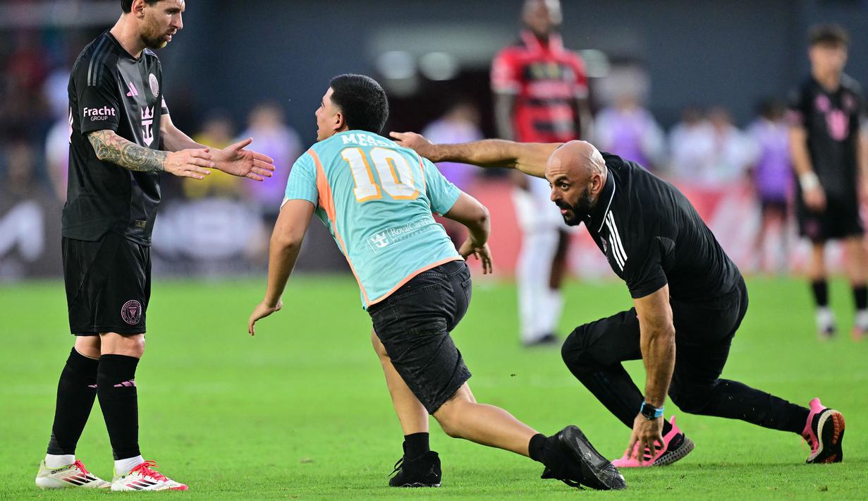 Pengawal Lionel Messi, Yassine Cheuko (kanan) berusaha bangkit setelah terjatuh saat menangkap seorang penyusup lapangan dalam laga persahabatan antara Inter Miami melawan Sporting San Miguelito di Stadion Romeo Fernandez, Panama, Amerika, Senin (03/02/2025) waktu setempat. (AFP/Martin Bernetti)