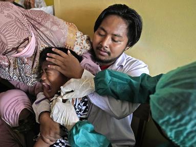 Orangtua, guru, dan polisi mencoba menenangkan seorang siswa saat dia disuntik pada kampanye vaksinasi COVID-19 di sebuah sekolah untuk anak-anak berkebutuhan khusus di Depok, Jawa Barat, Selasa (11/1/2022). Kampanye vaksinasi ini dilakukan oleh Polri. (AP Photo/Dita Alangkara)