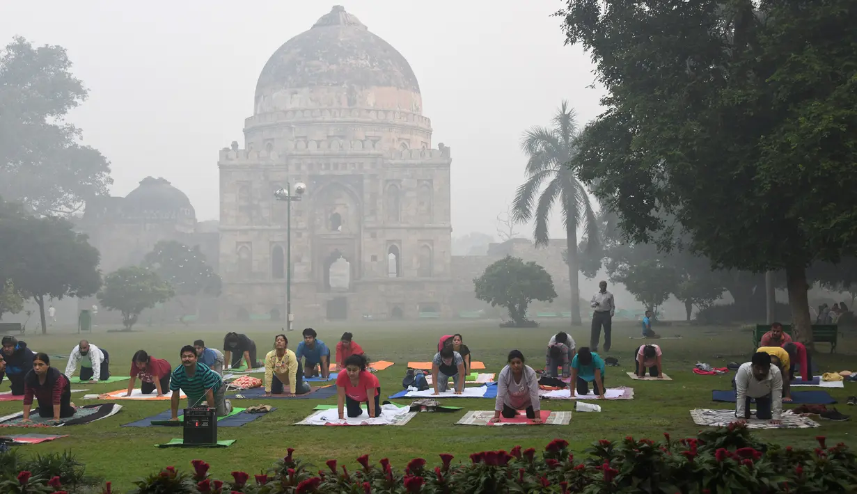 Warga berlatih yoga di Lodhi Gardens di tengah kondisi kabut asap tebal di New Delhi (30/10). Tingkat kabut melonjak selama musim dingin di Delhi, ketika kualitas udara sering melampaui tingkat aman Organisasi Kesehatan Dunia. (AFP Photo/Dominique Faget)