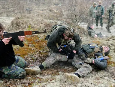 Warga sipil berlatih menembak sementara rekannya melakukan pengobatan prajurit yang terluka saat mengikuti sesi pelatihan militer oleh Right Sector dekat Lviv, Ukraina, 24 Februari 2023. (AP Photo/Mykola Tys)