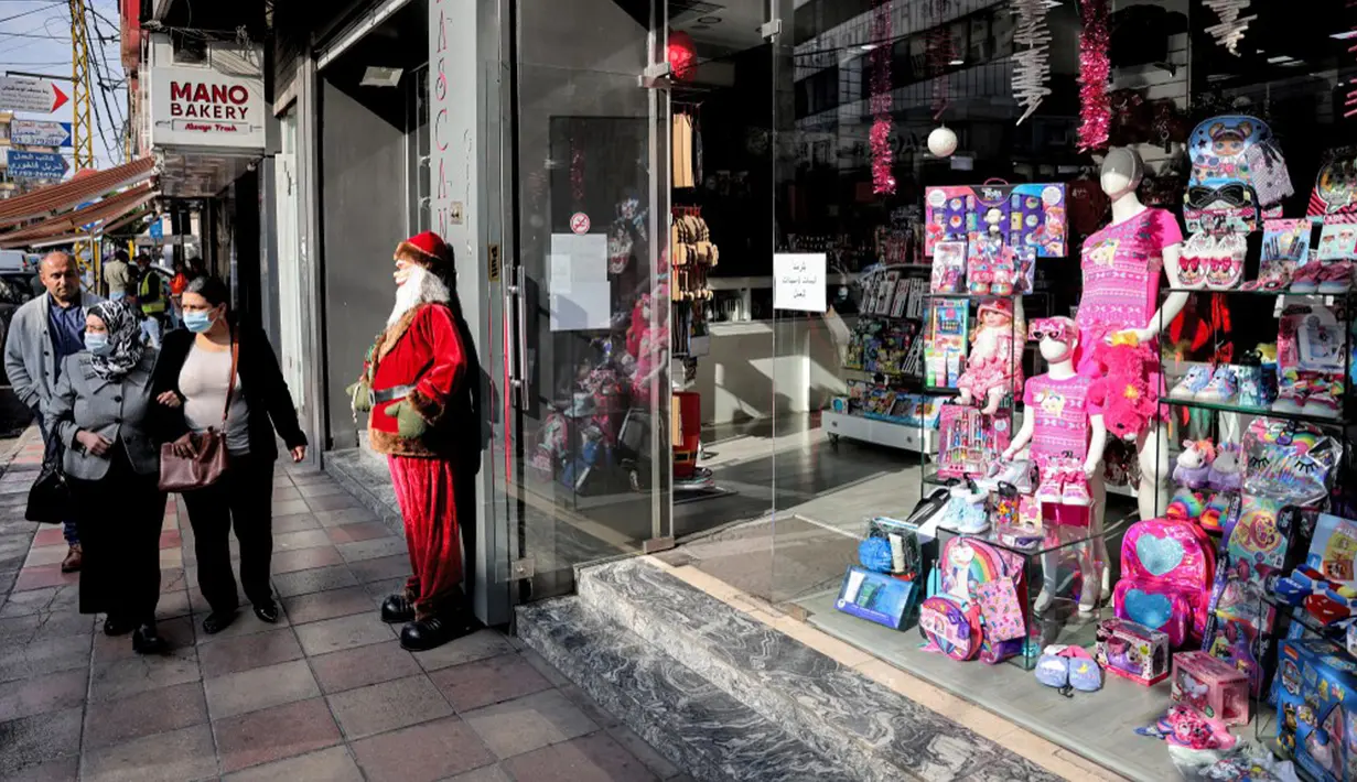 Warga berjalan melewati patung Santo Nikolas (Bapa Natal atau Sinterklas) di luar pintu masuk toko mainan di kawasan Burj Hammoud, Beirut, Lebanon, 14 Desember 2021. Semarak jelang Natal yang biasa terjadi di Beirut, tak lagi terasa tahun ini karena krisis keuangan di Lebanon. (JOSEPH EID/AFP)