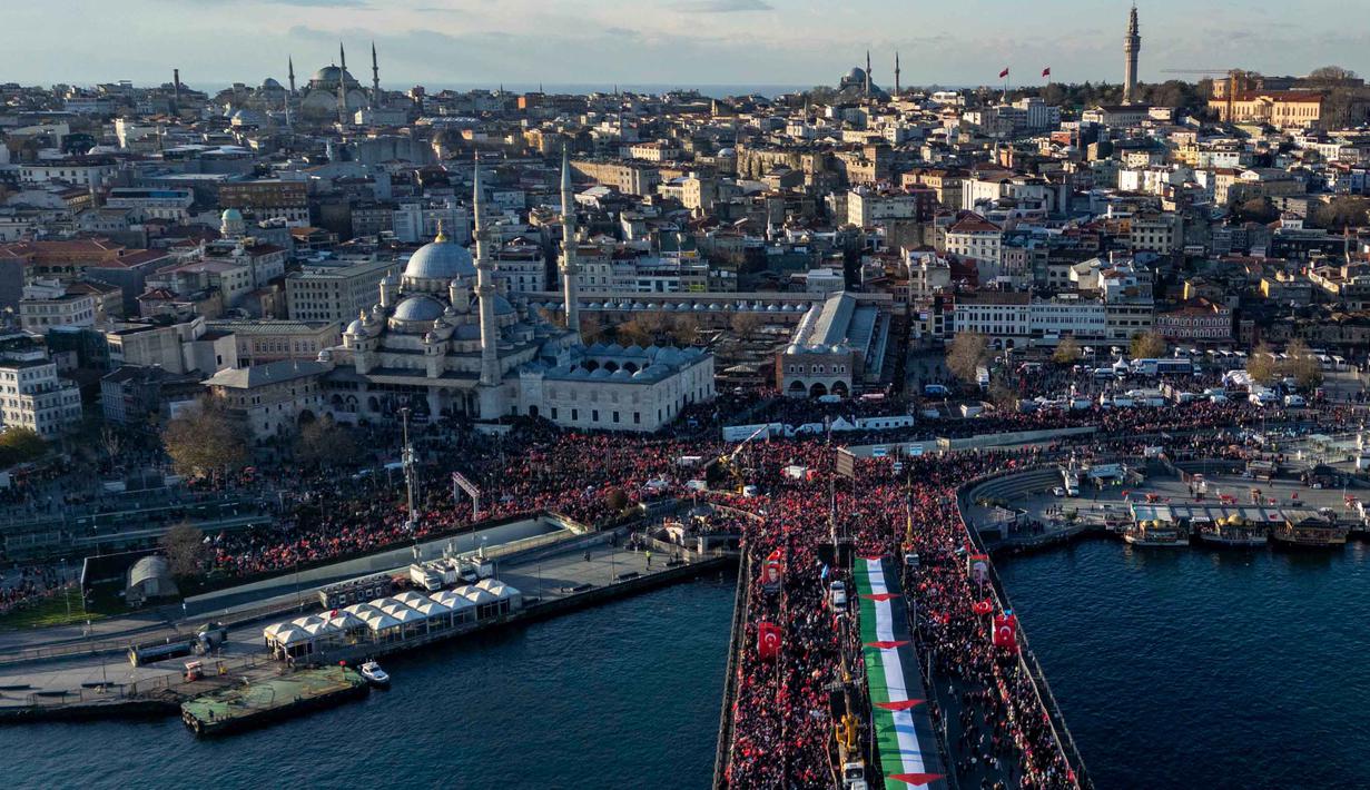 Saat ini, ada lebih dari 1,5 juta warga Palestina tinggal di tenda-tenda darurat dalam kondisi serba kekurangan di tengah kehancuran luas serta ancaman musim dingin. Tampak foto udara menunjukkan ribuan orang yang berdemonstrasi menunjukkan solidaritas mereka dengan rakyat Palestina di tengah perang yang sedang berlangsung antara Israel dan kelompok Hamas di wilayah Gaza, di Jembatan Galata, Istanbul, Turki pada 1 Januari 2026. (Yasin AKGUL/AFP)