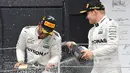 Pembalap Mercedes Lewis Hamilton merayakan kemenangan bersama rekannya Valtteri Botas di atas podium setelah berhasil memenangkan GP Inggris di sirkuit Silverstone, (16/7). (AFP Photo/Ben Stansall)