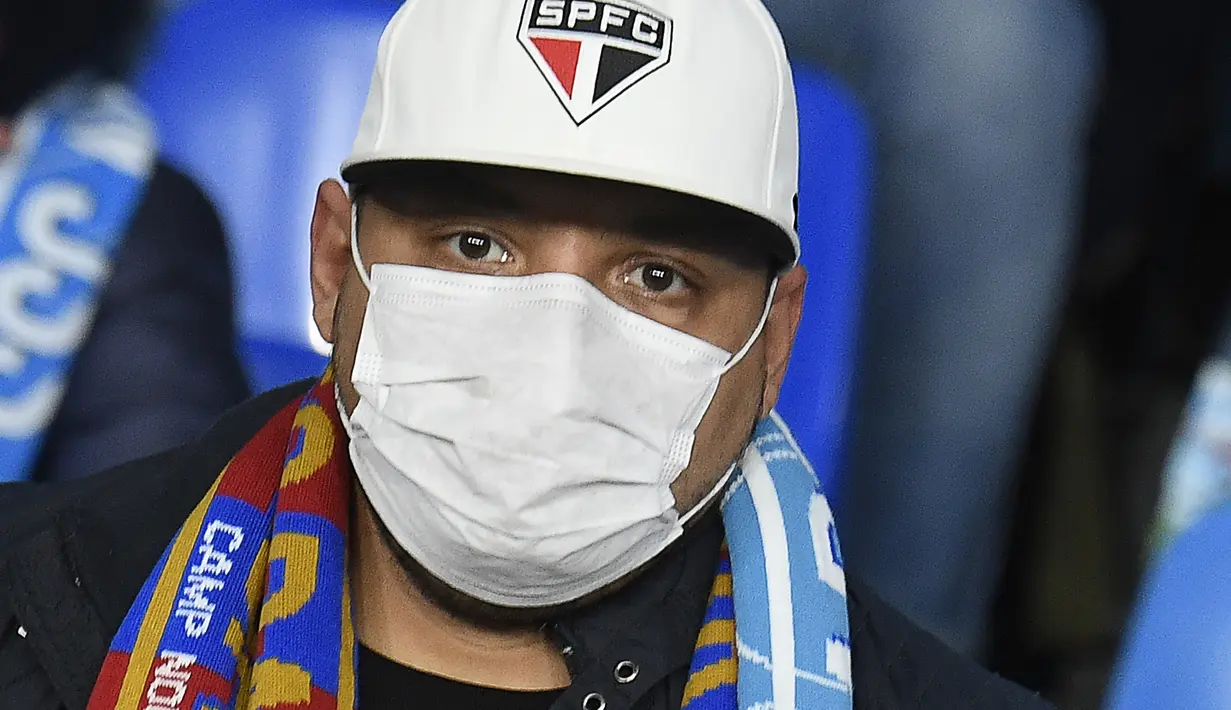 Seorang suporter Napoli  mengenakan masker menunggu dimulainya pertandingan antara Napoli dan Barcelona di Stadion San Paolo di Naples, Italia, Selasa, (25/2/2020). Dalam laga ini, Barcelona berhasil menanhan tuan rumah Napoli 1-1. (AFP Photo/Filippo Monteforte)