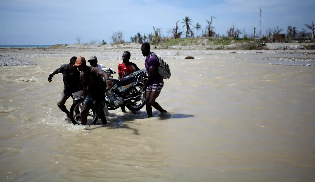 Sejumlah pria membantu warga menggotong sepeda motornya menyeberangi sungai di Les Anglais, 10 Oktober 2016. Selain merusak ribuan rumah, badai Matthew di Haiti juga memutus jembatan yang merupakan akses utama warga. (REUTERS/Andres Martinez Casares)