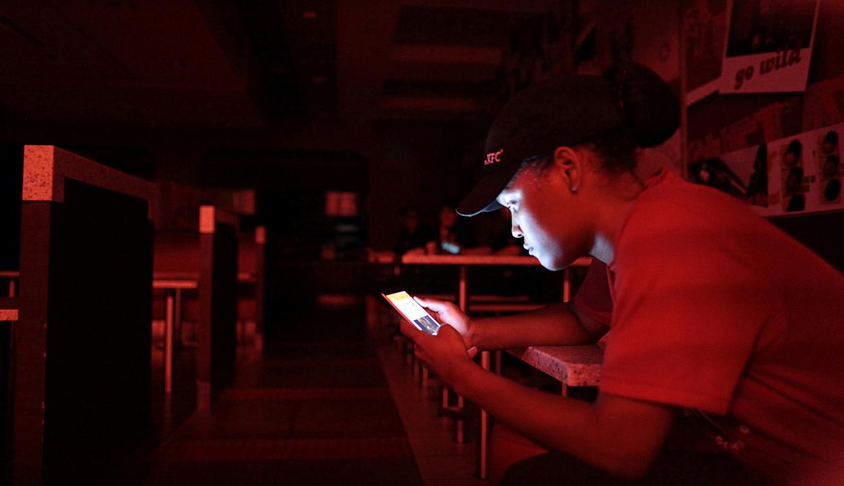 Seorang karyawan di restoran cepat saji bermain ponsel selama pemadaman listrik di San Juan, Puerto Rico, Rabu (21/9). Kebakaran telah memutus dua jalur transmisi listrik dan mengakibatkan kegagalan penyaluran tenaga ke seluruh pulau. (REUTERS/Alvin Baez)