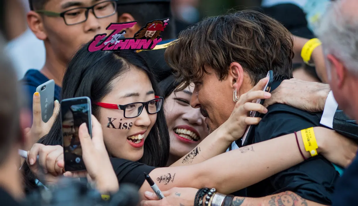 Aktor Johnny Depp saat memeluk dua penggemarnya saat tiba menghadiri pemutaran perdana film Disney "Pirates of the Caribbean: Dead Men Tell No Tales" di Shanghai (11/5). (AFP Photo/Johannes Eiselle) 