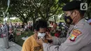 Polisi memasangkan masker untuk pengunjung yang berwisata di Taman Mini Indonesia Indah (TMII), Jakarta, Sabtu (15/5/2021). Selama libur Lebaran, pengelola TMII memberlakukan protokol kesehatan secara ketat. (Liputan6.com/Faizal Fanani)