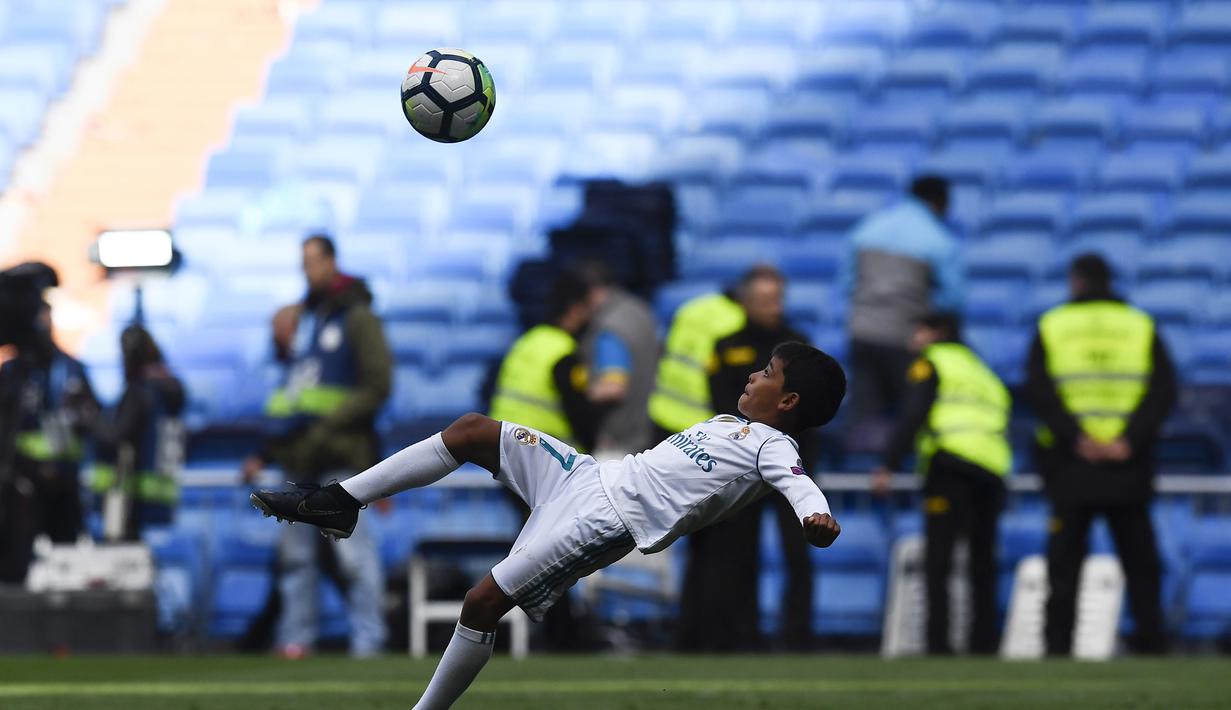 Putra dari Cristiano Ronaldo bersiap melakukan tendangan salto saat menemani sang ayah di Stadion Santiago Bernabeu, Madrid, Minggu (8/4/2018). Tendangan ini mirip seperti saat CR 7 membobol gawang Juventus. (AFP/Gabriel Bouys).